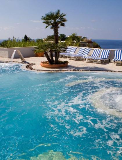 Piscina con idromassaggio, vista mare, lettini e sole splendente.