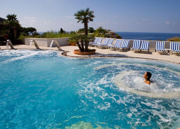 Piscina con idromassaggio, vista mare, lettini e palme: relax e tranquillità.